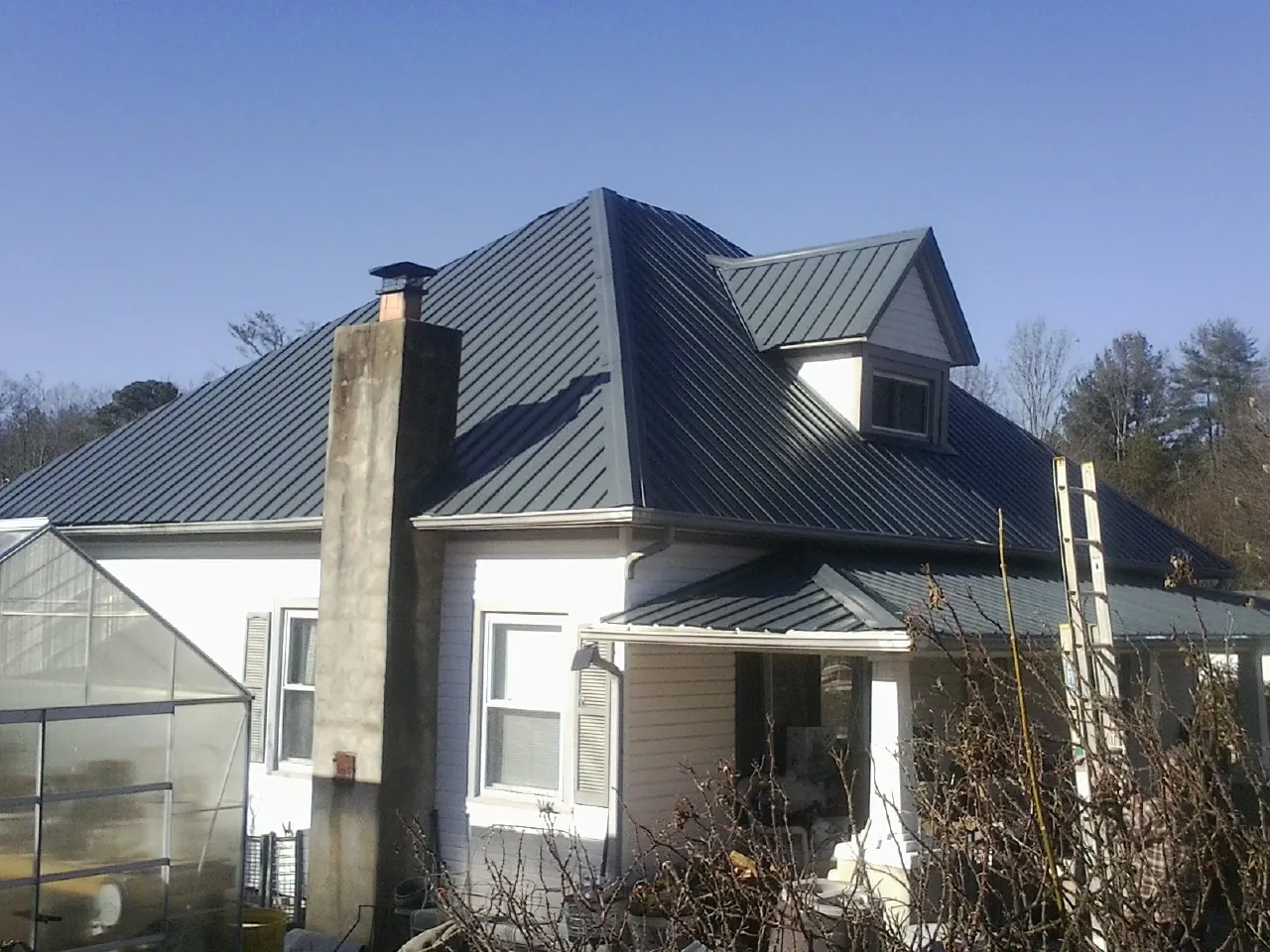 Dark blue standing seam metal roof on a white farmhouse with dormer — Slate & Tile Roof Repair by Roofing Brothers in New Pine Creek