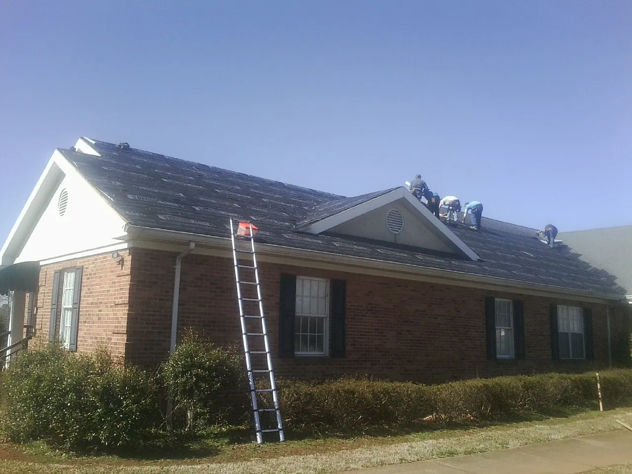 Crew tearing shingles off a brick ranch roof with a ladder set — Emergency Roof Repair work by our crew in New Pine Creek