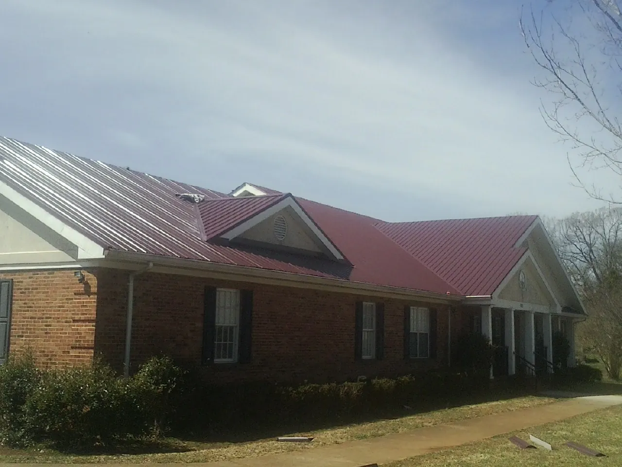 Red metal roof with gabled entries on a long brick building, from a Hail Damage Roof Repair job in New Pine Creek