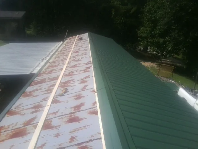 Old rusted panels beside newly installed green metal roofing — Wind Damage Roof Repair by Roofing Brothers in New Pine Creek