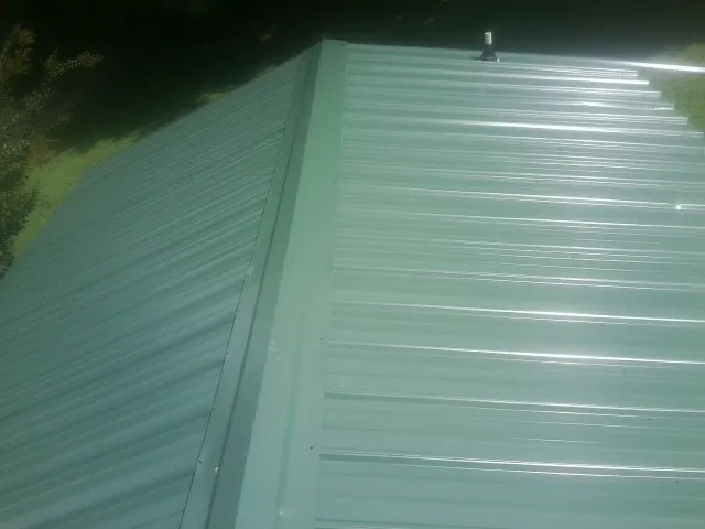 New green metal panels meeting at the ridge of a roof — Flat Roof Repair work by our crew in New Pine Creek