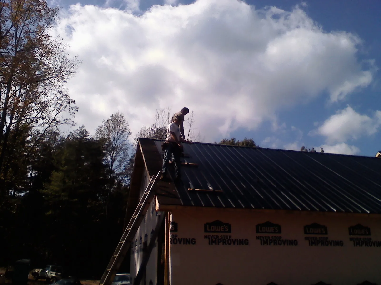 Roofer fastening dark metal panels high against a cloudy sky, from a Roof Inspection job in New Pine Creek