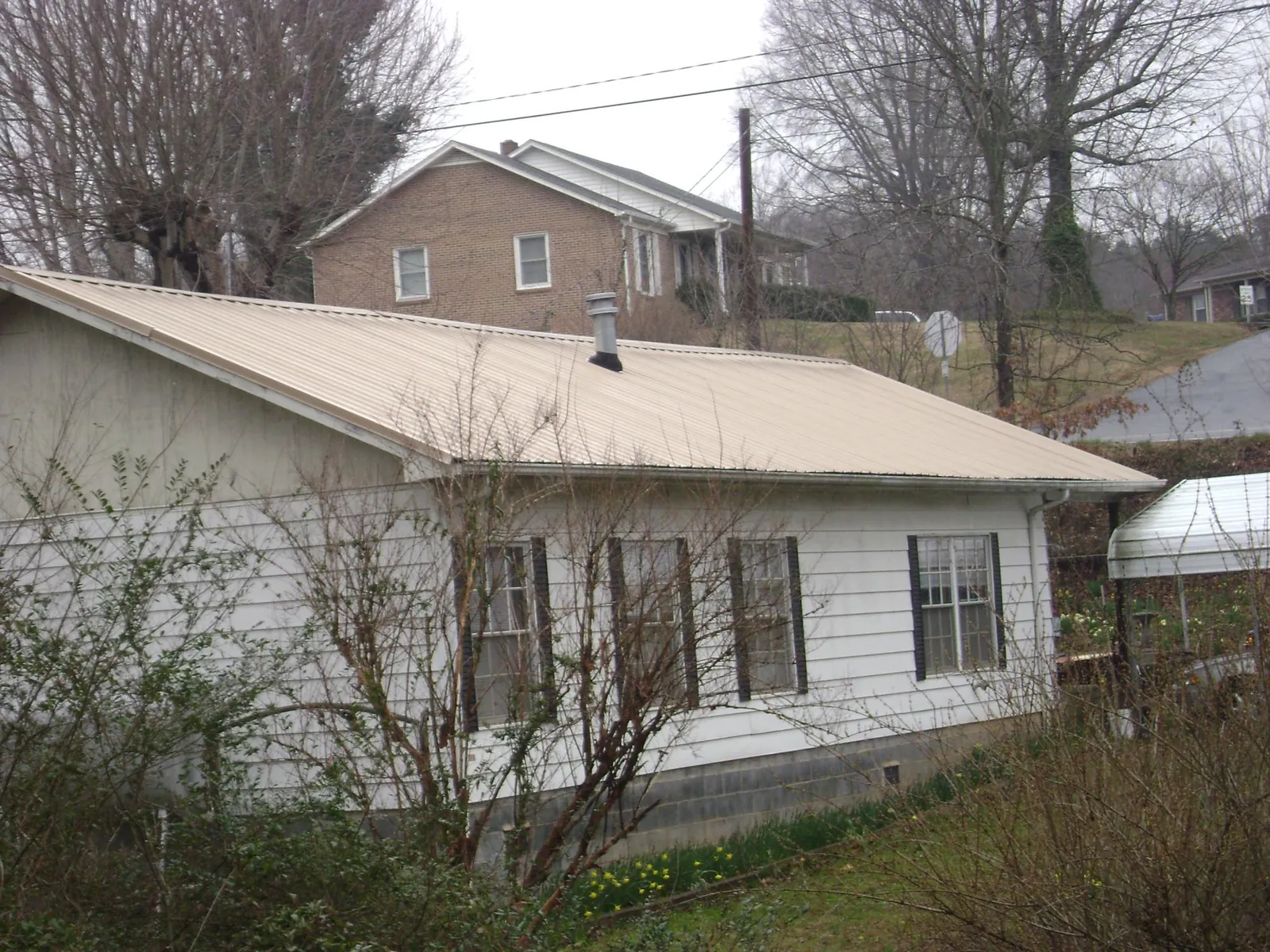 Tan metal roof on a white sided house set into a hillside — Commercial Roofing by Roofing Brothers in New Pine Creek